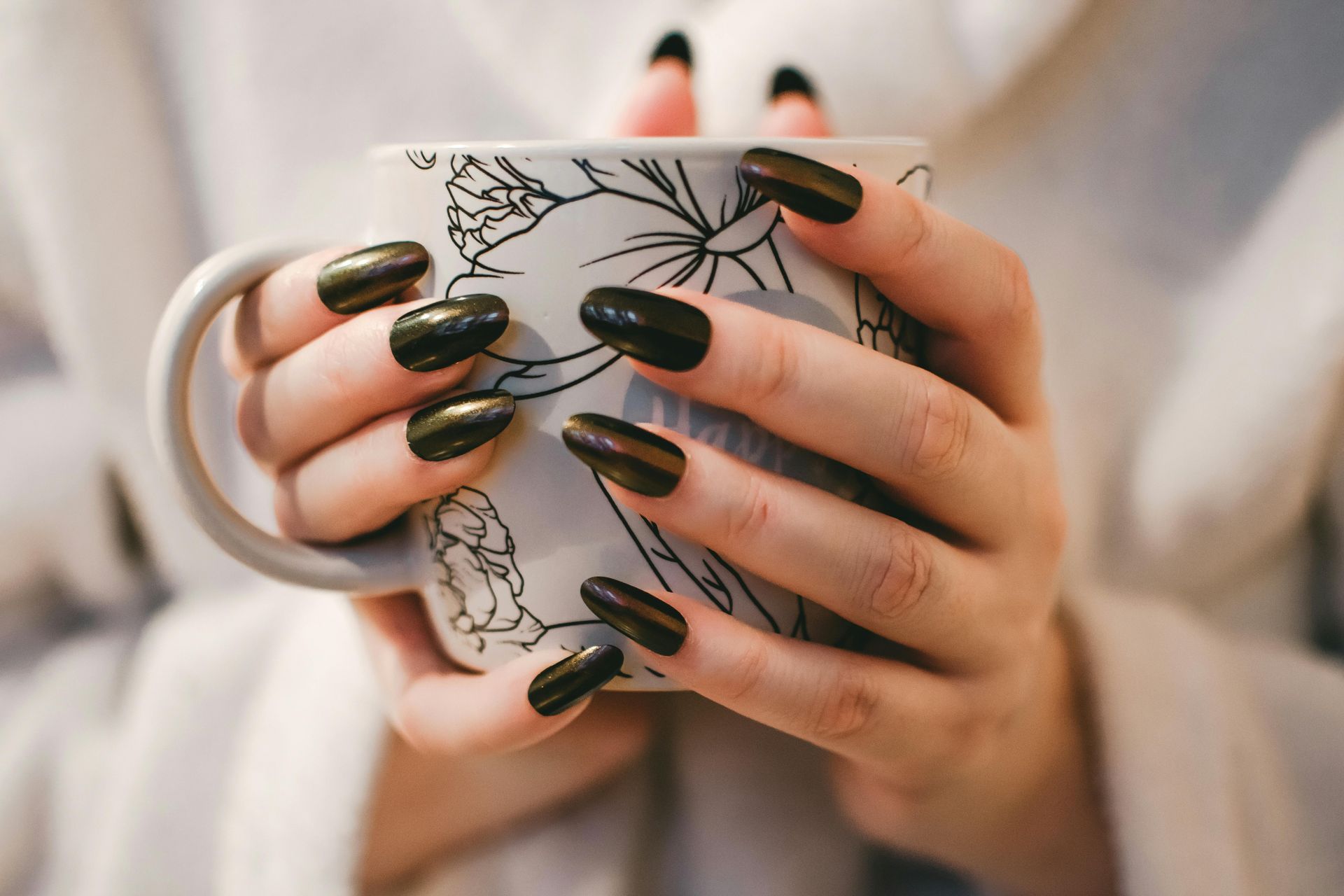A woman with long black nails is holding a cup of coffee.
