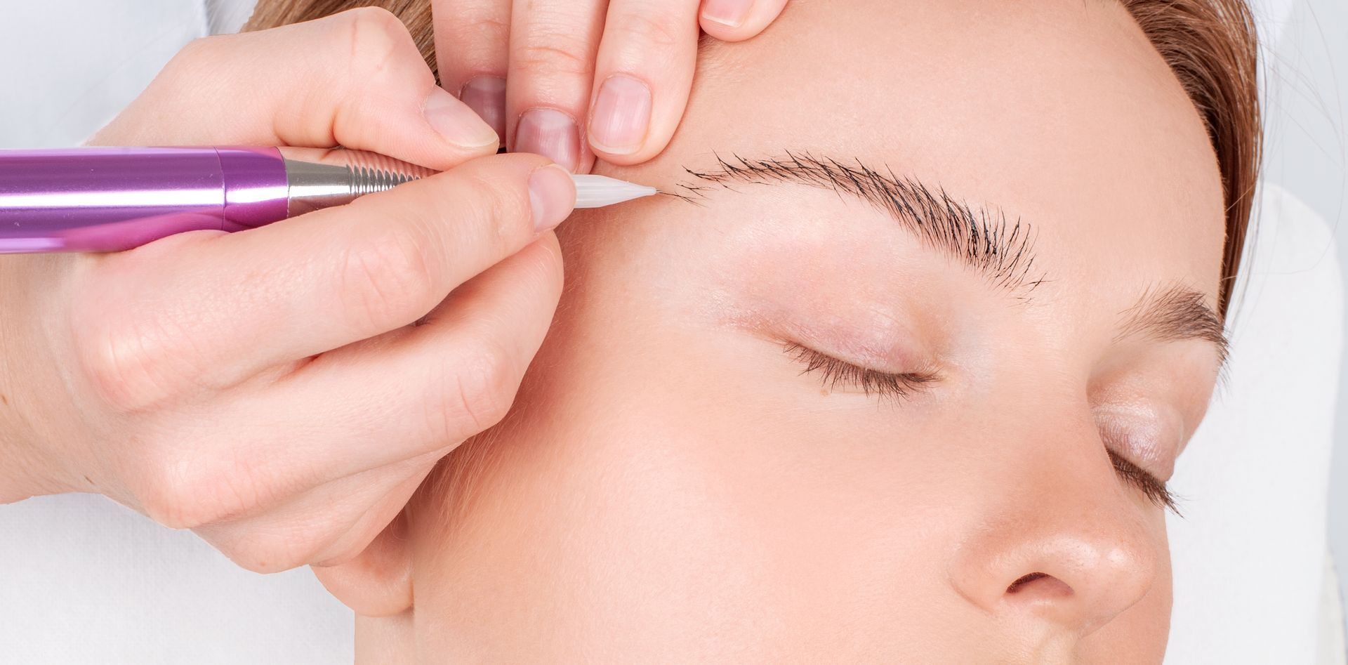 A woman is getting a permanent makeup tattoo on her eyebrows.