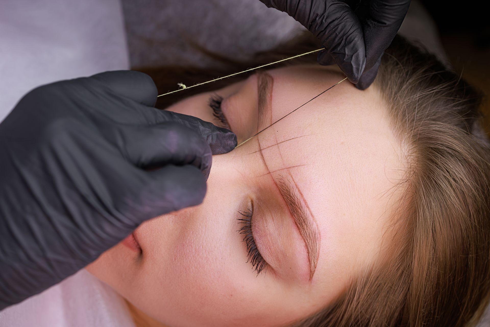 A woman is getting her eyebrows drawn by a tattoo artist.