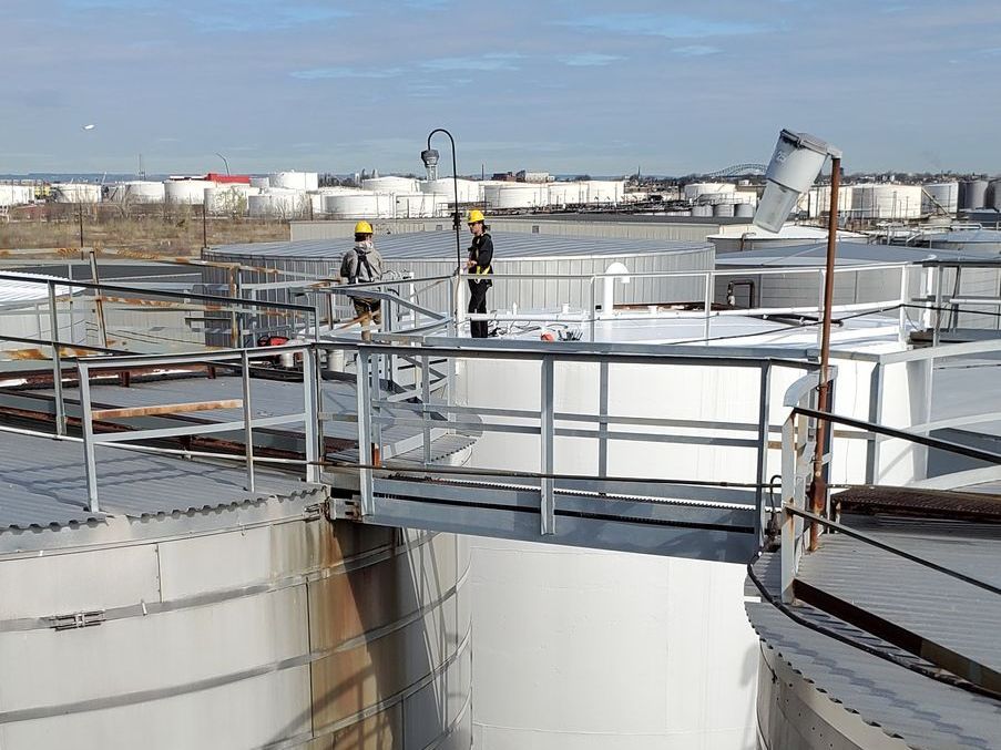 Two men are standing on a bridge over a large tank.