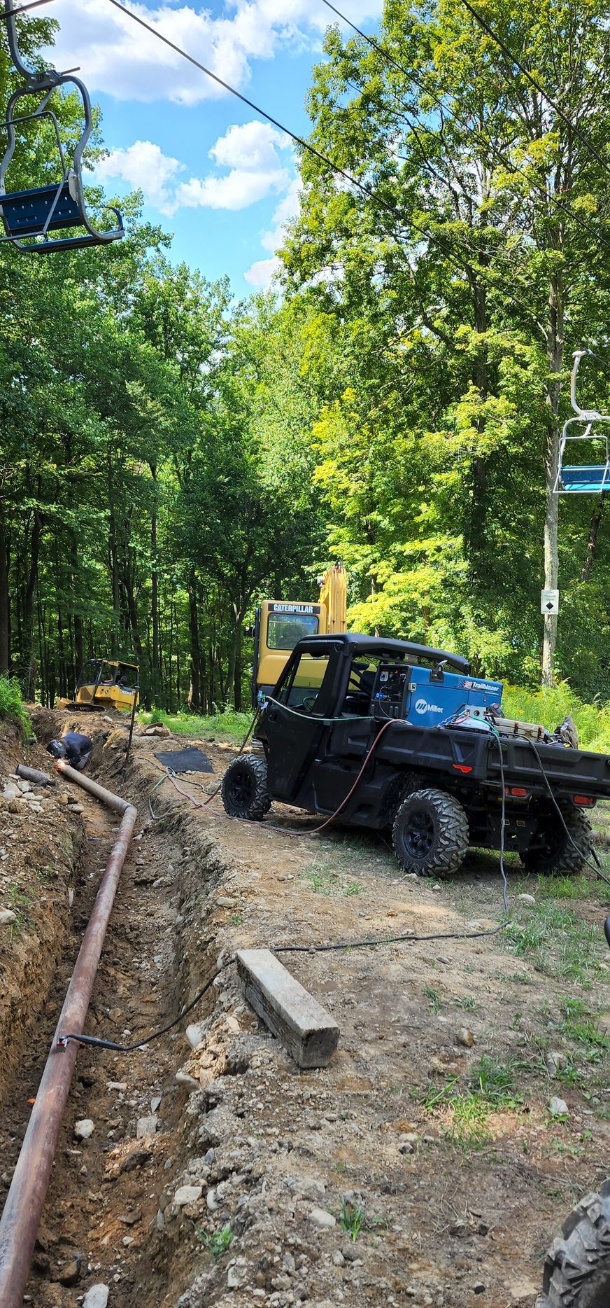 A atv is parked on the side of a dirt road next to a ski lift.