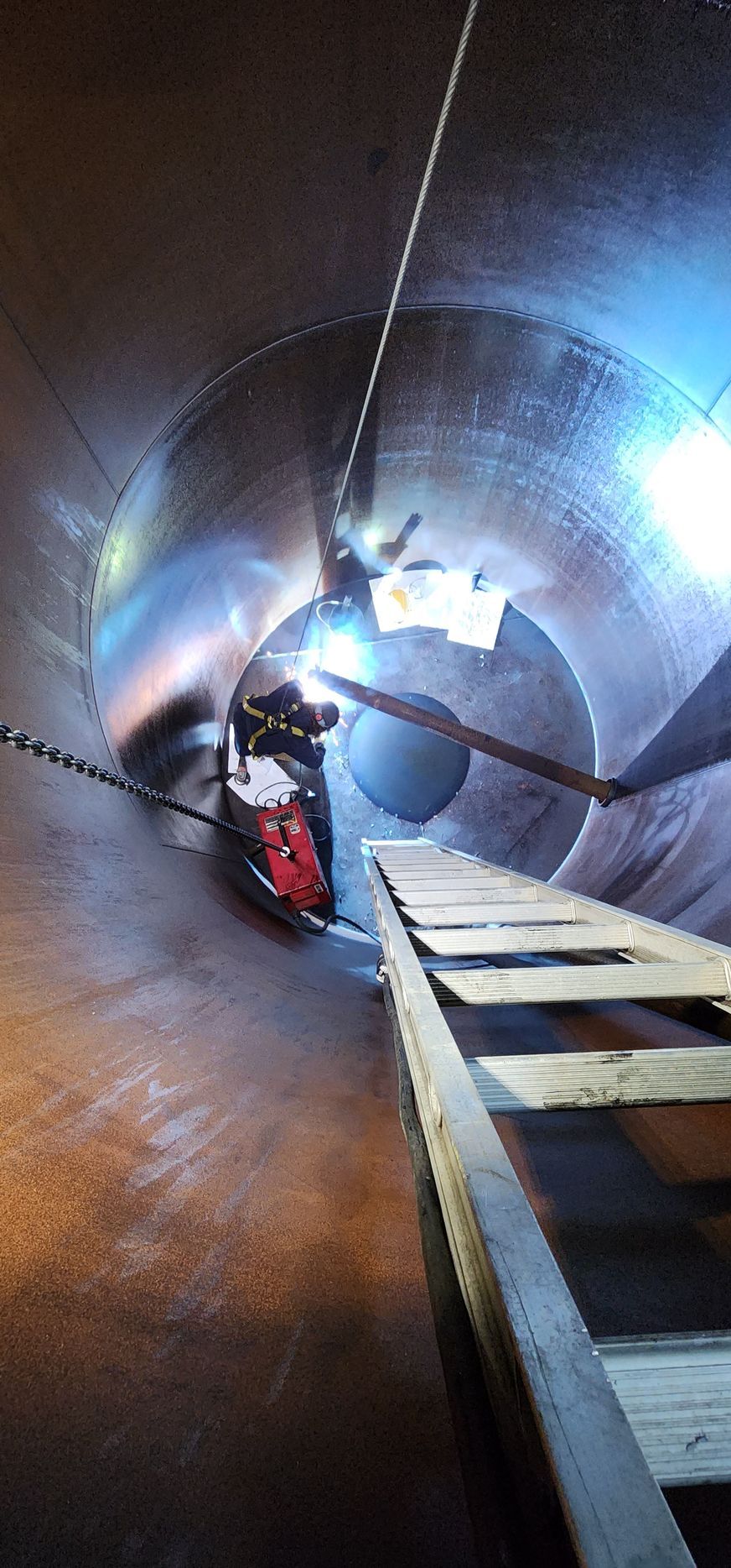 A man is welding a large pipe in a tunnel.