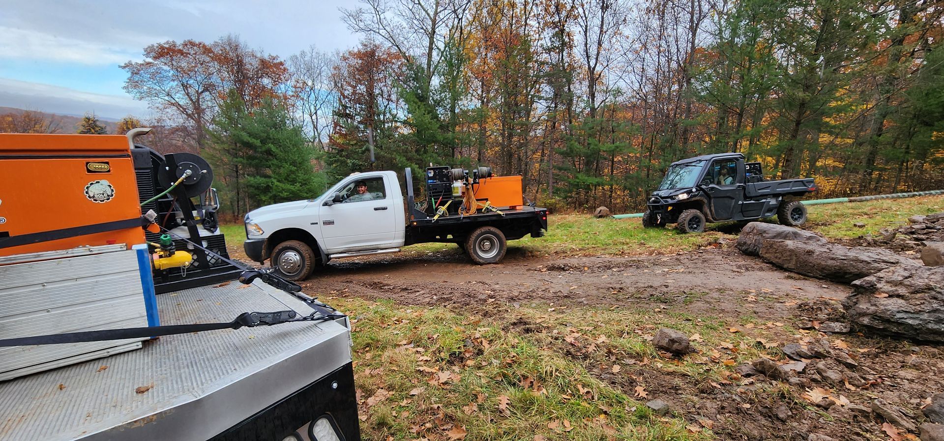 Two trucks are parked in a field with trees in the background.