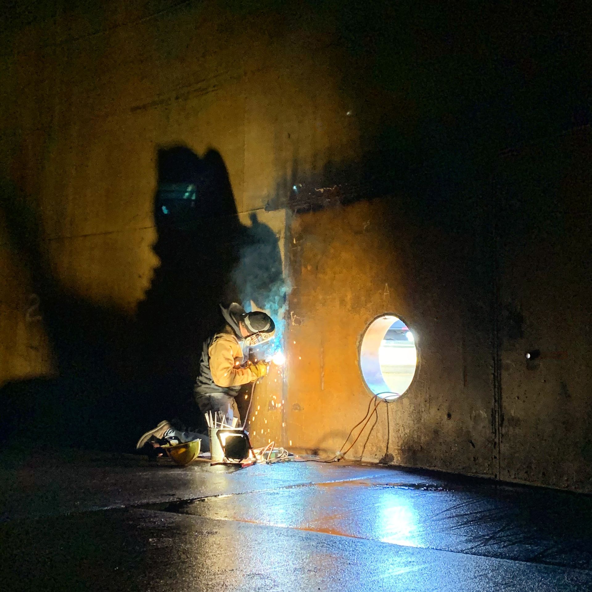 A man is welding a hole in a wall in a dark room