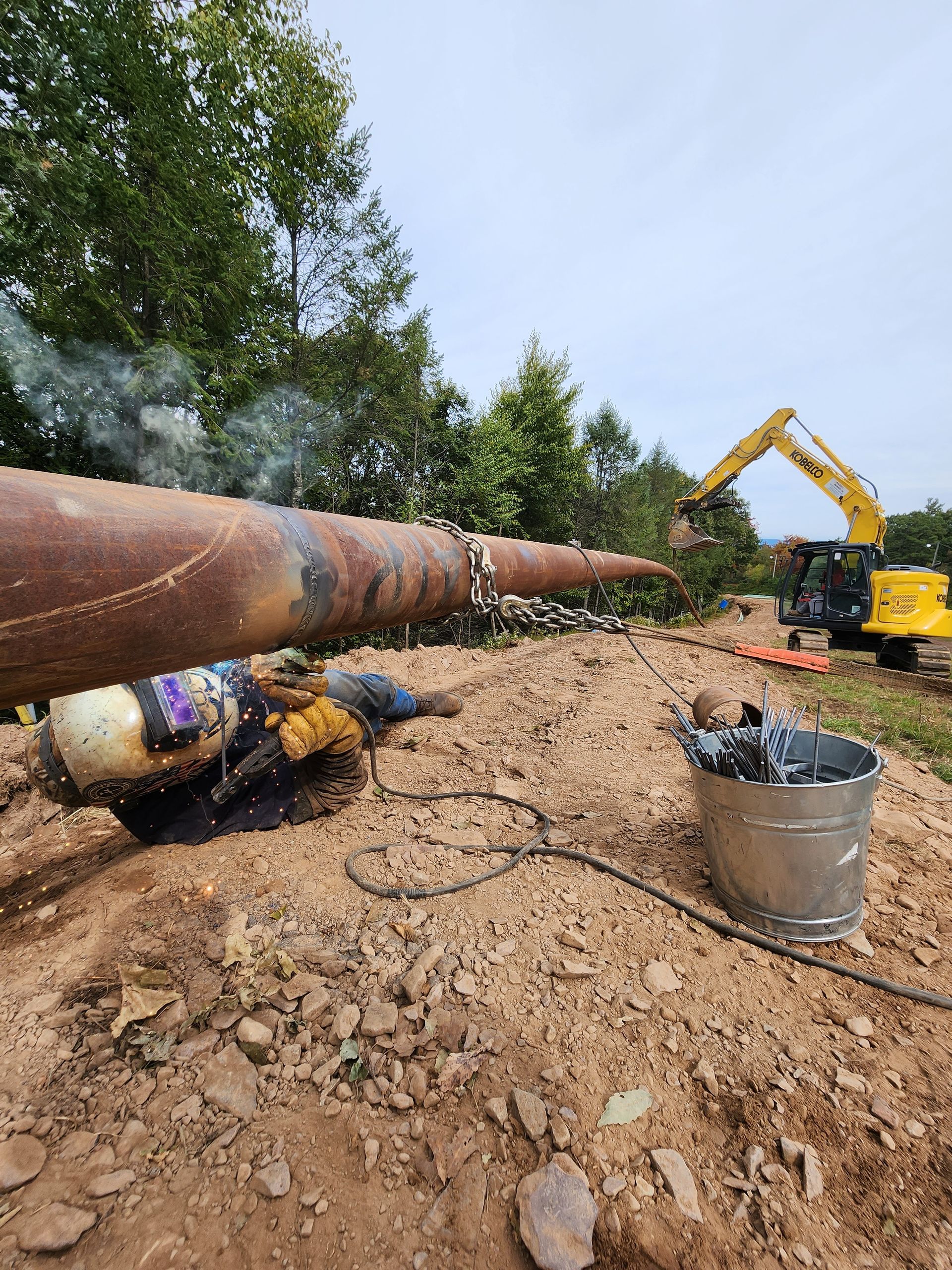 A man is welding a large pipe in the dirt.