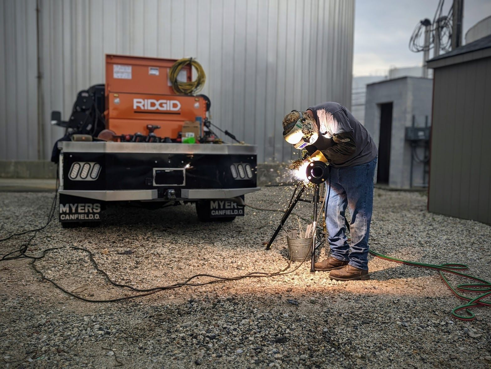 A man is welding a piece of metal in front of a ridgid truck.