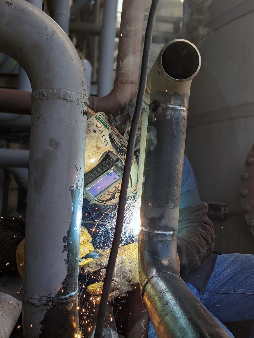 A man is welding a pipe in a factory.
