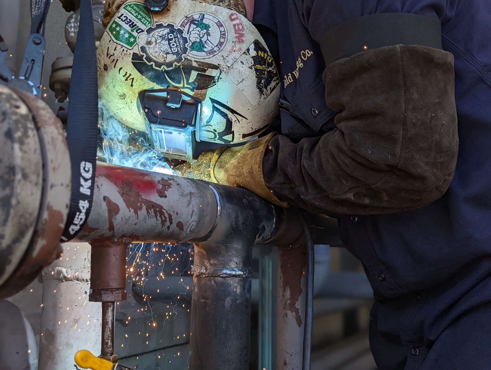 A man is welding a pipe with a strap that says 4 kg on it