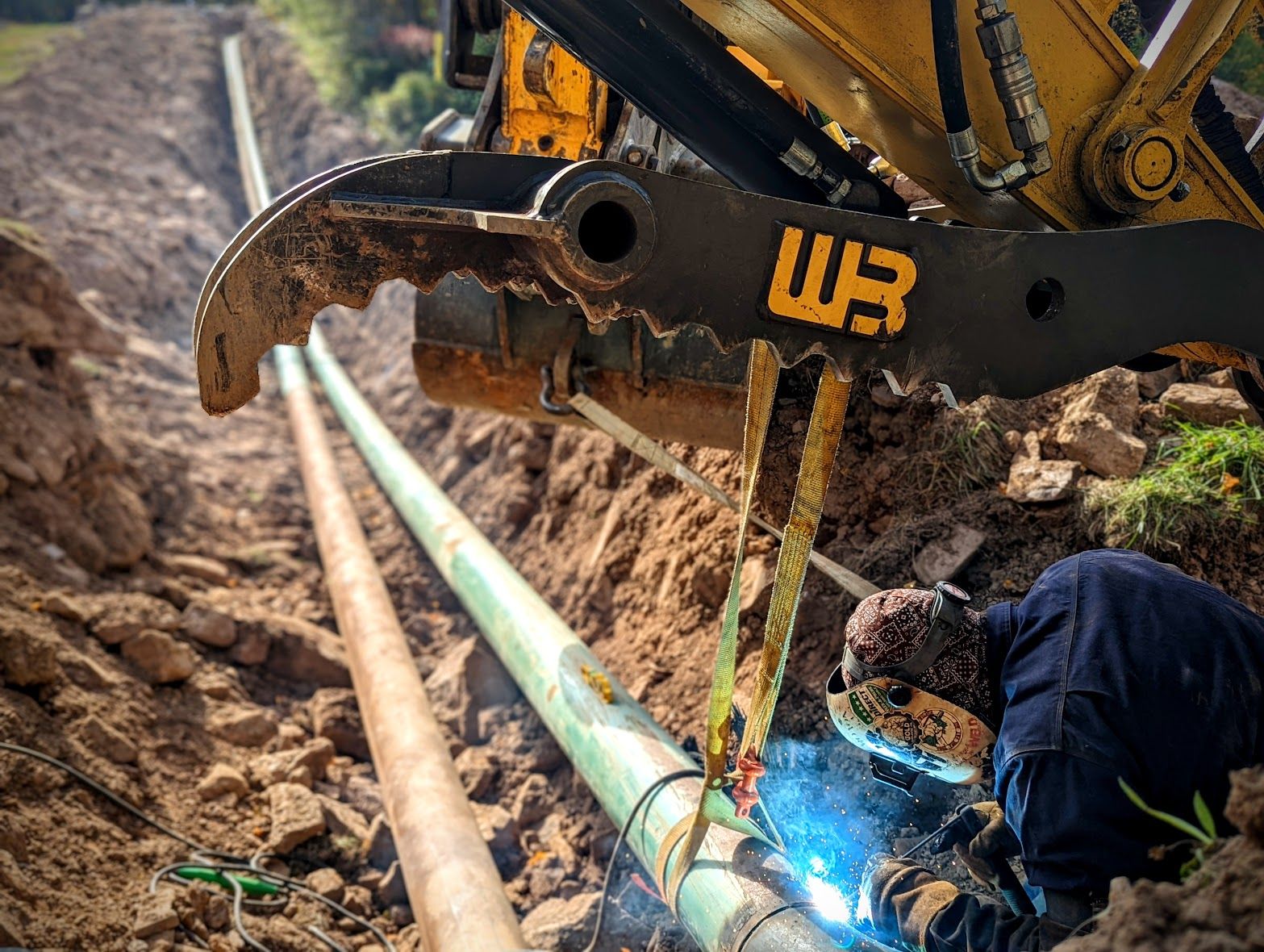 A man is welding a pipe in the dirt.