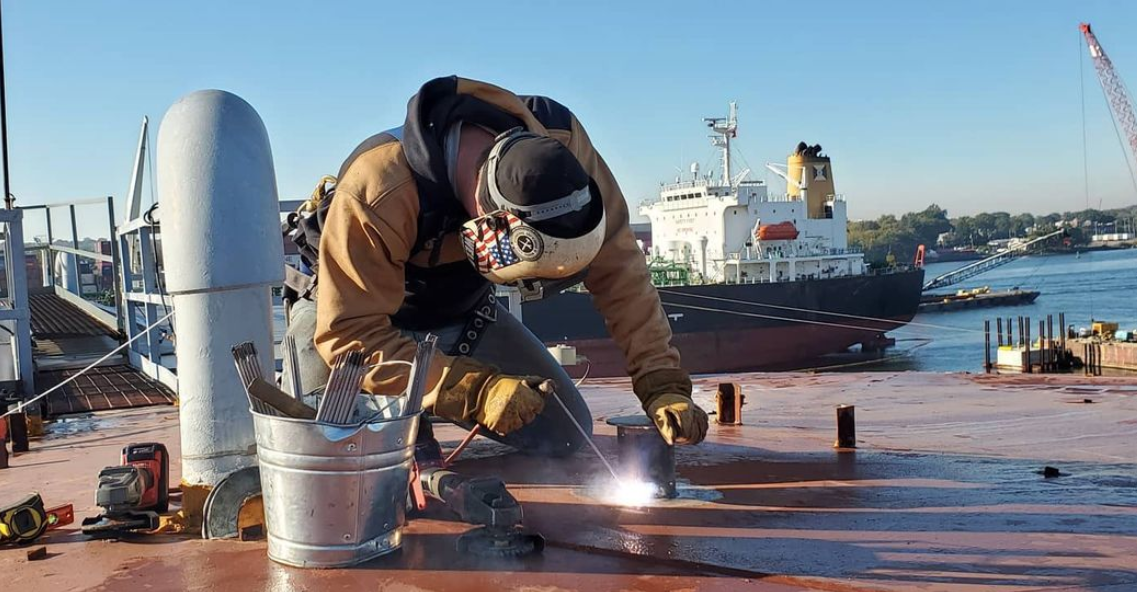 A man is welding a piece of metal on a boat.