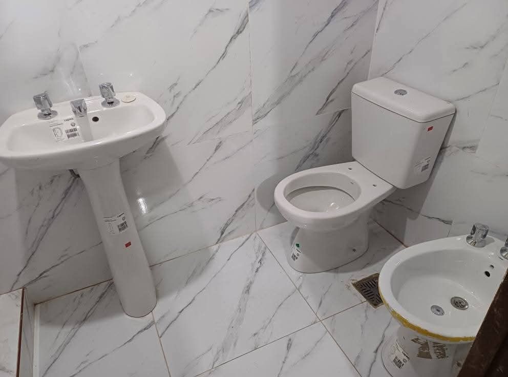 Baño con lavabo de pedestal blanco, inodoro y bidé. Azulejos con diseño de mármol en paredes y suelo.