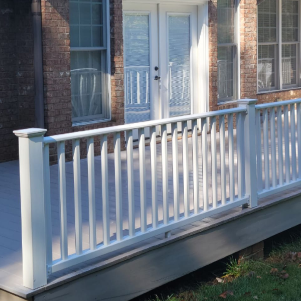 a deck with a white railing in front of a brick house
