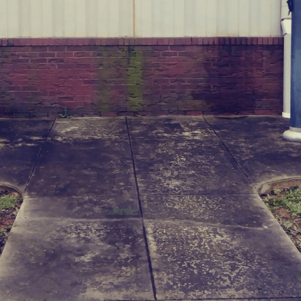 a dirty concrete walkway with a brick wall in the background .