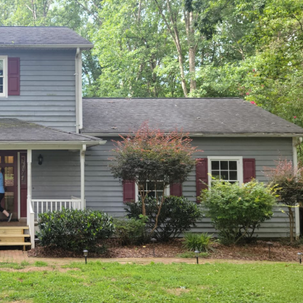 a gray house with red shutters and a porch surrounded by trees .
