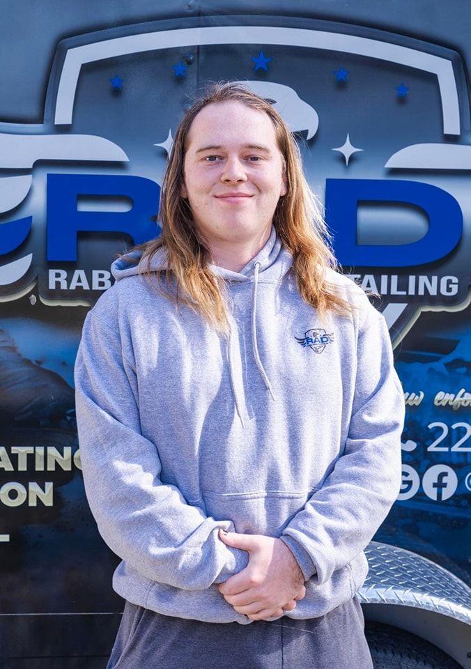 A man with long hair is standing in front of a trailer.