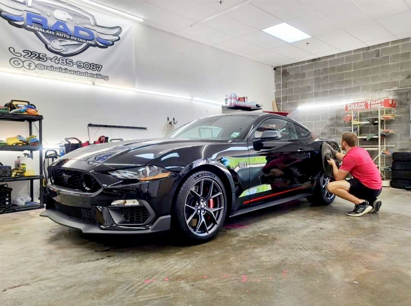 A man is working on a black mustang in a garage.