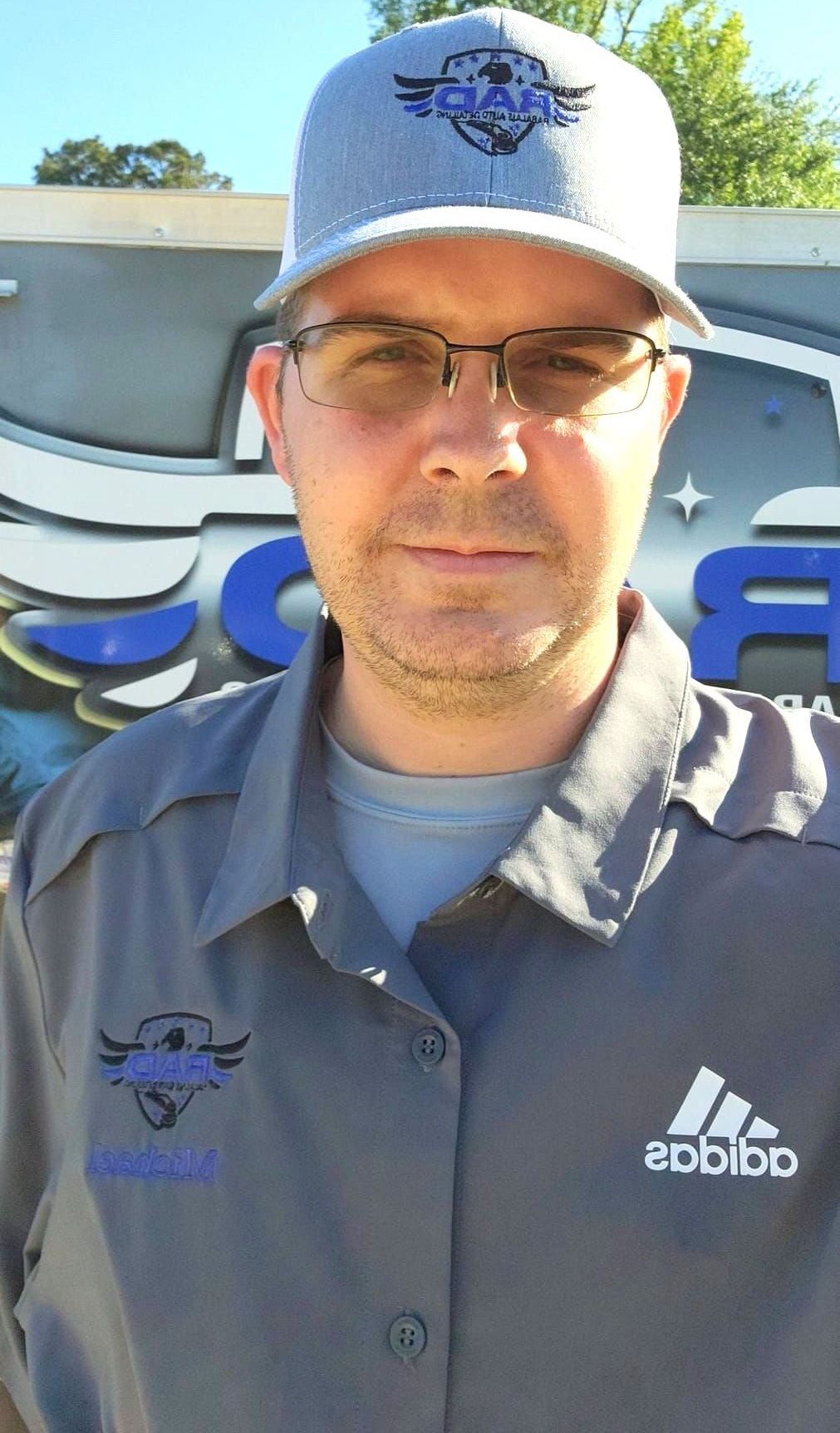 A man wearing a hat and glasses is standing in front of a building.
