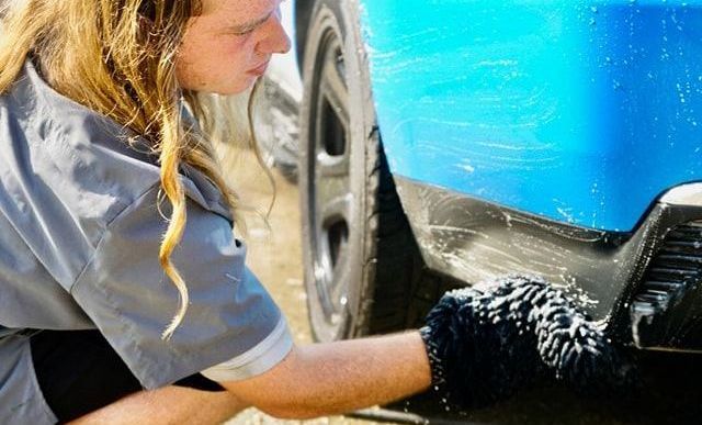 A man is washing a blue car with a glove.