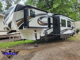 A large white and black rv is parked in a dirt lot in front of a house.