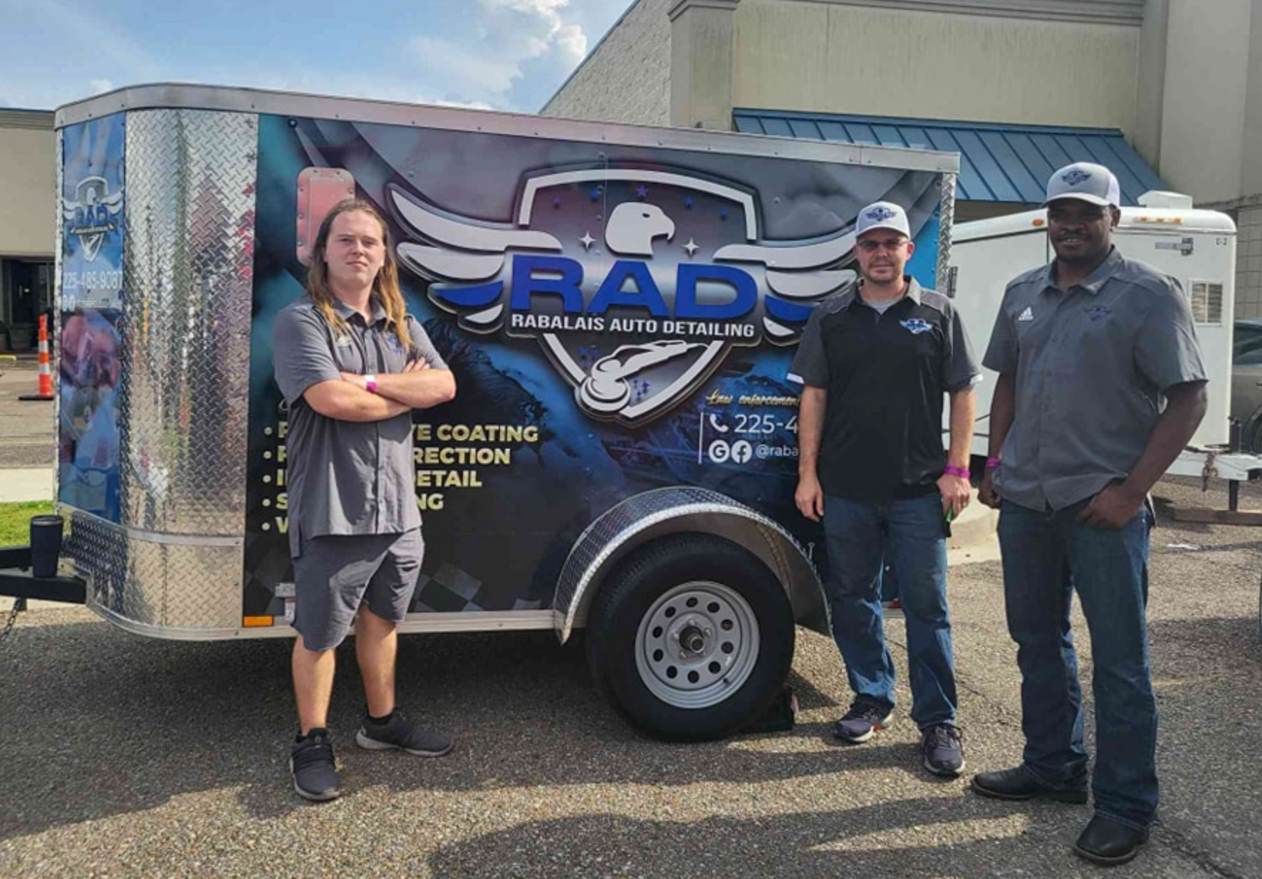 Three men are standing in front of a trailer that says rad