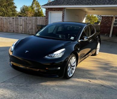 A black tesla model 3 is parked in front of a house