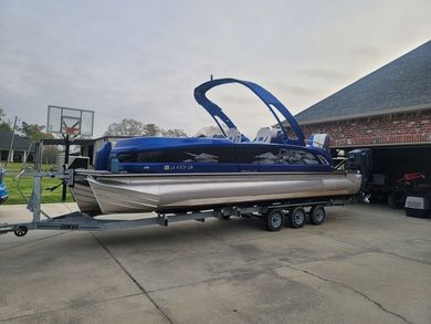 A blue pontoon boat is parked on a trailer in front of a garage.