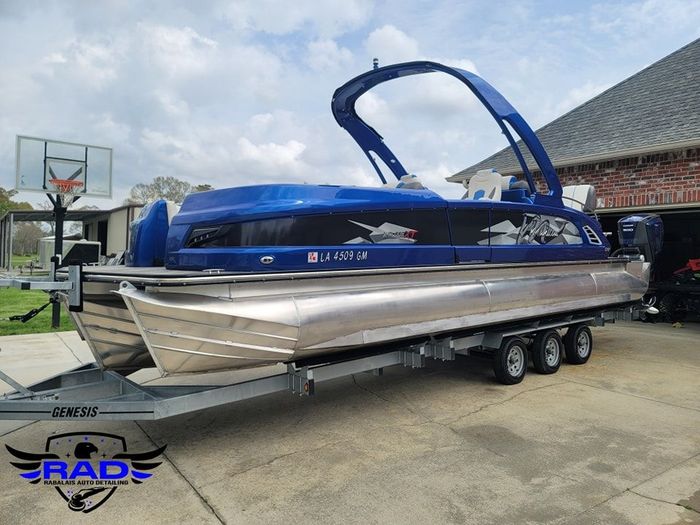 A blue pontoon boat is parked on a trailer in front of a house.