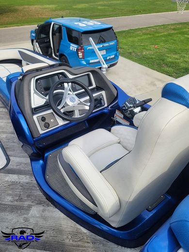 A blue boat with a steering wheel and seats is parked in a driveway.