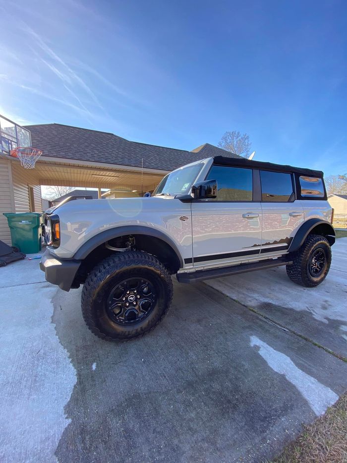 A white ford bronco is parked in front of a house in the snow.