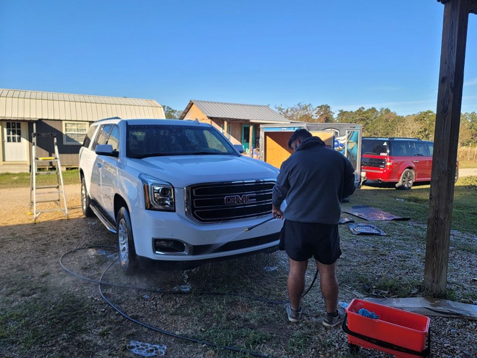 A man is washing a white suv in a yard.