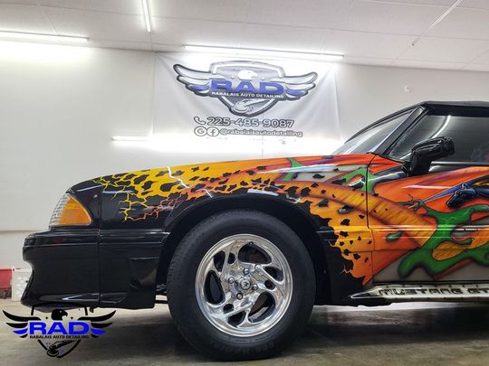 A colorful car is parked in front of a rad banner