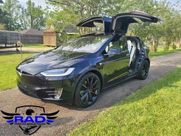 A black tesla model x with its doors open is parked on a dirt road.