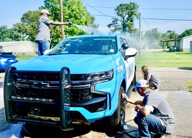 Two men are washing a blue truck with a hose.