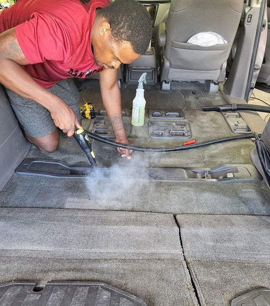 A man is cleaning the carpet of a car with a steam cleaner.