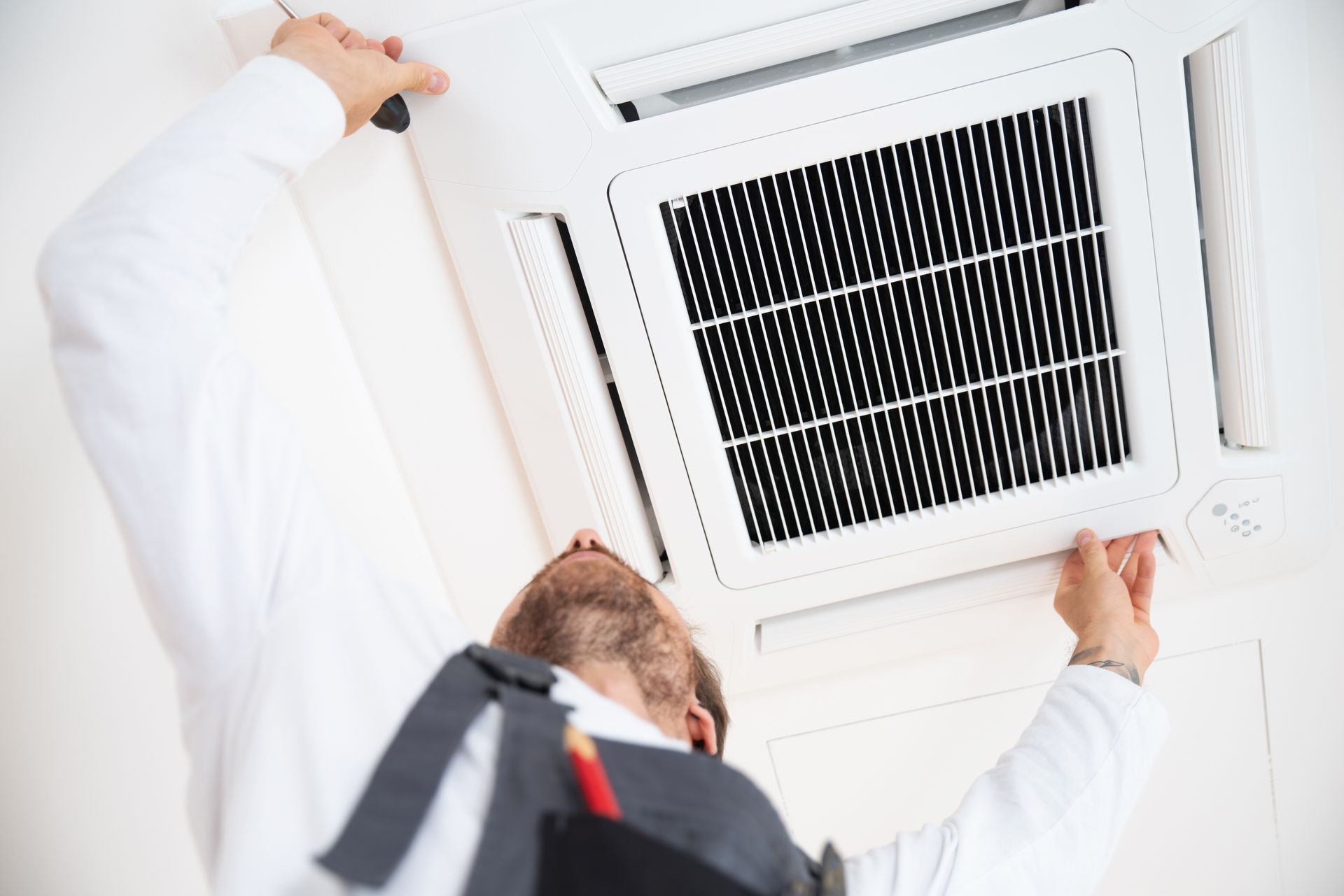 A man is working on a ceiling mounted air conditioner.