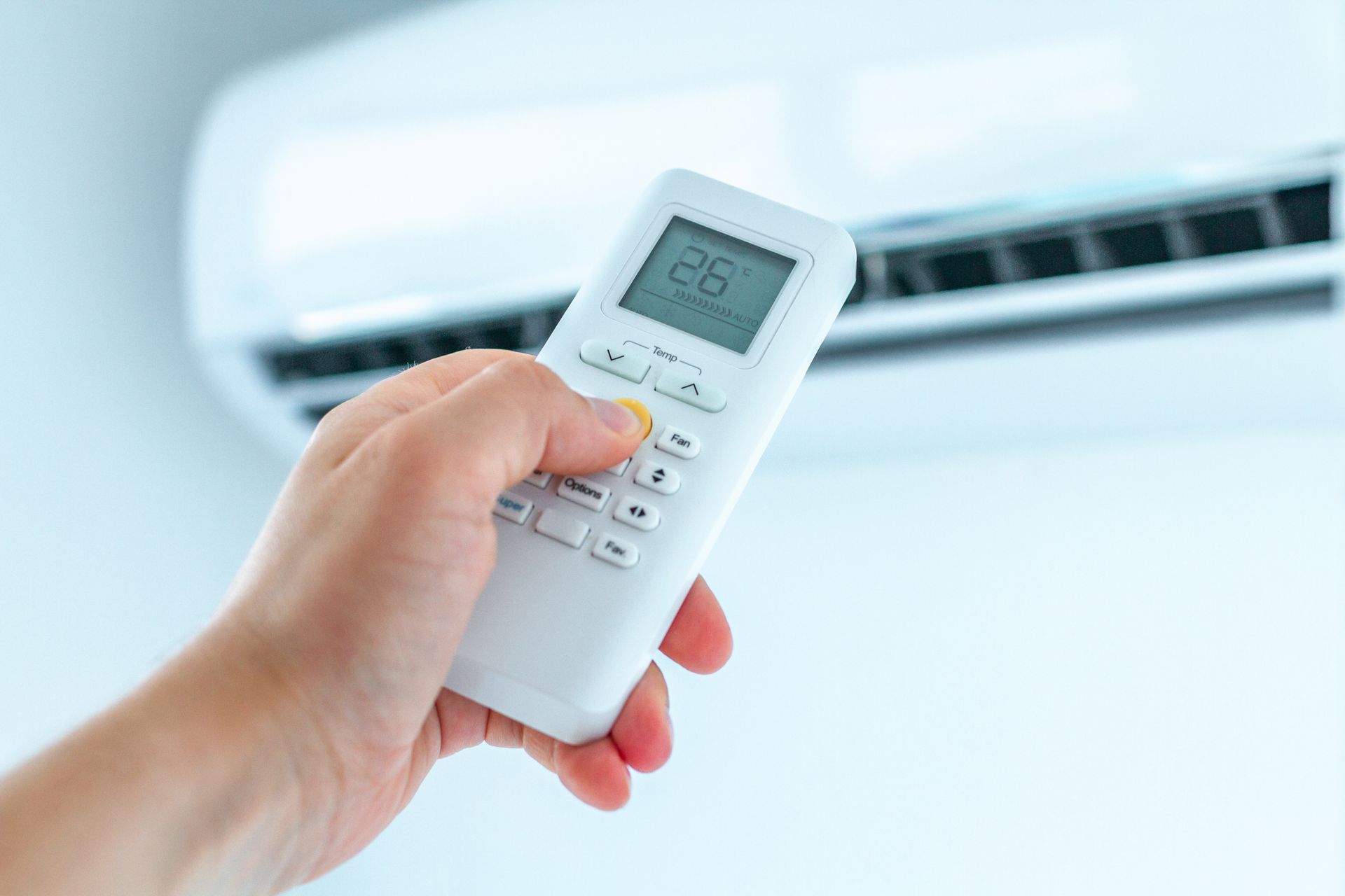 A person is holding a remote control in front of an air conditioner.