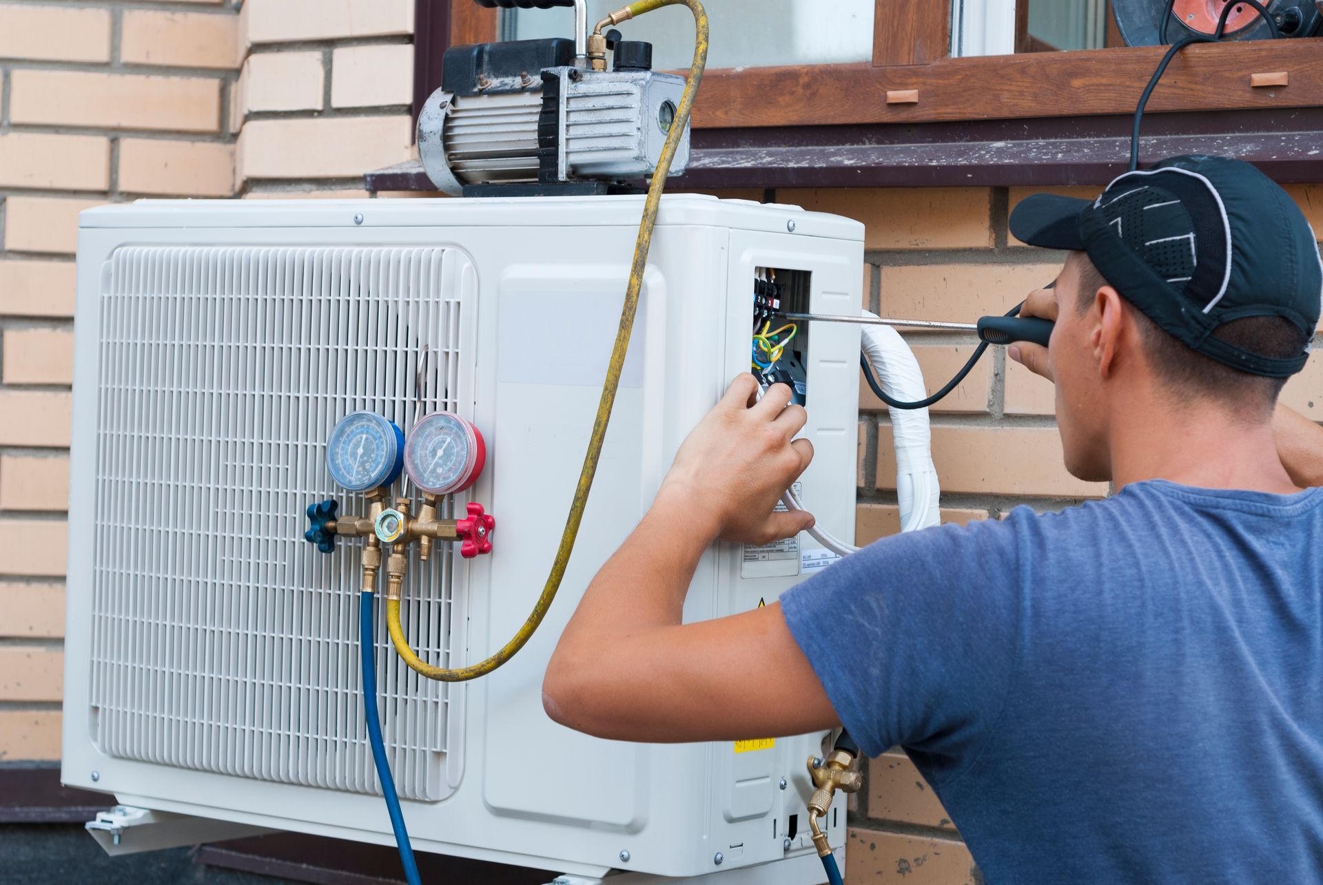 A man is working on an air conditioner outside of a brick building.