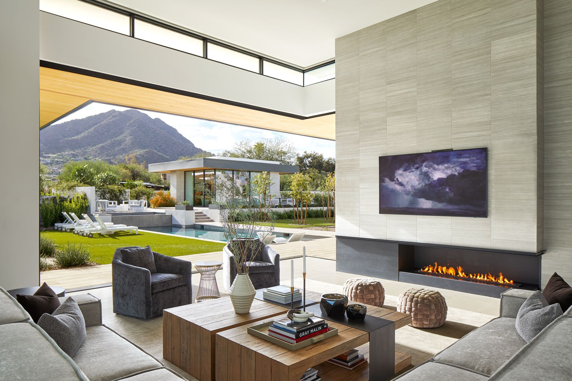 Living room with fireplace, TV, and open view of pool and mountains.