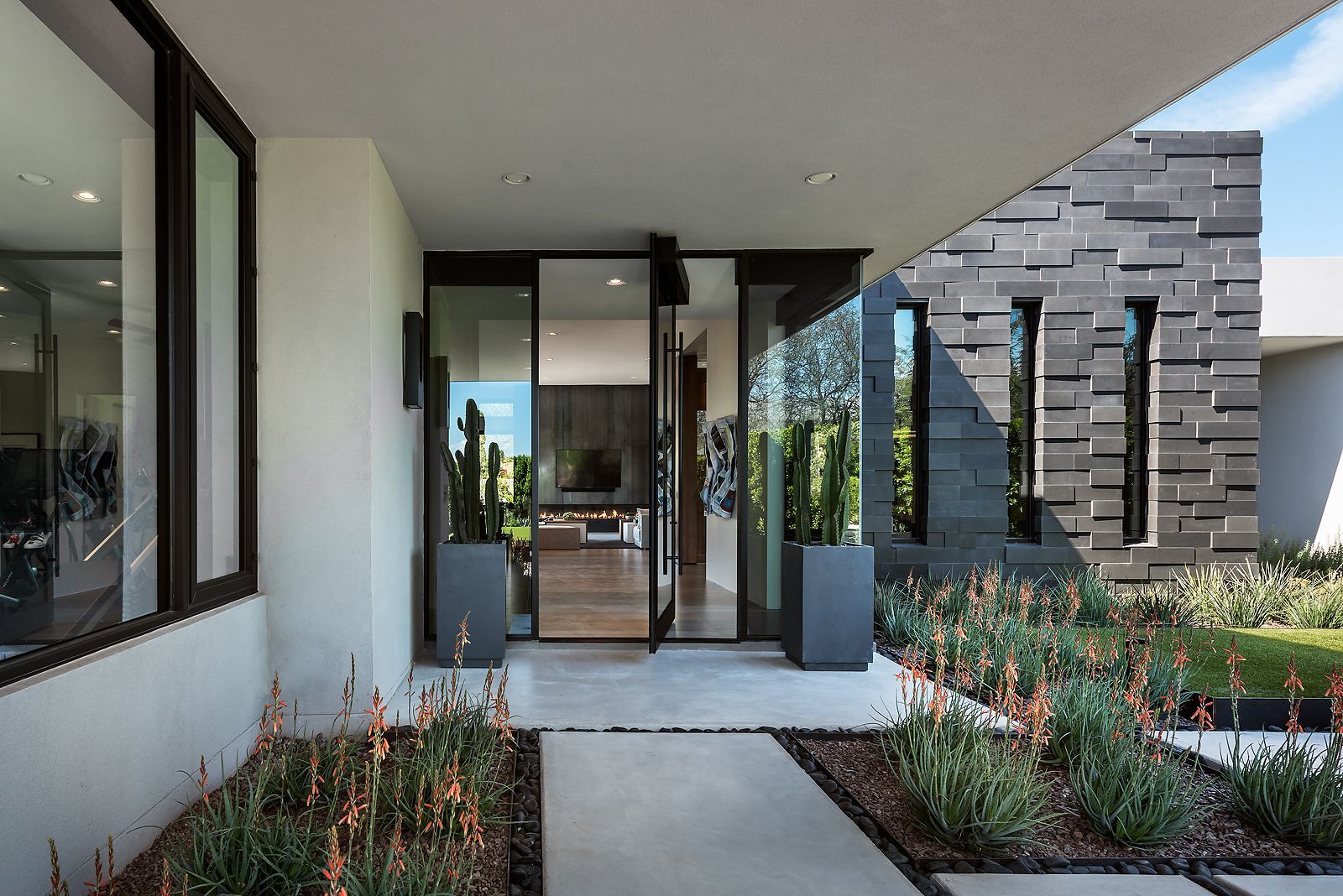 Modern home entrance with glass doors, stone wall, and desert landscaping.