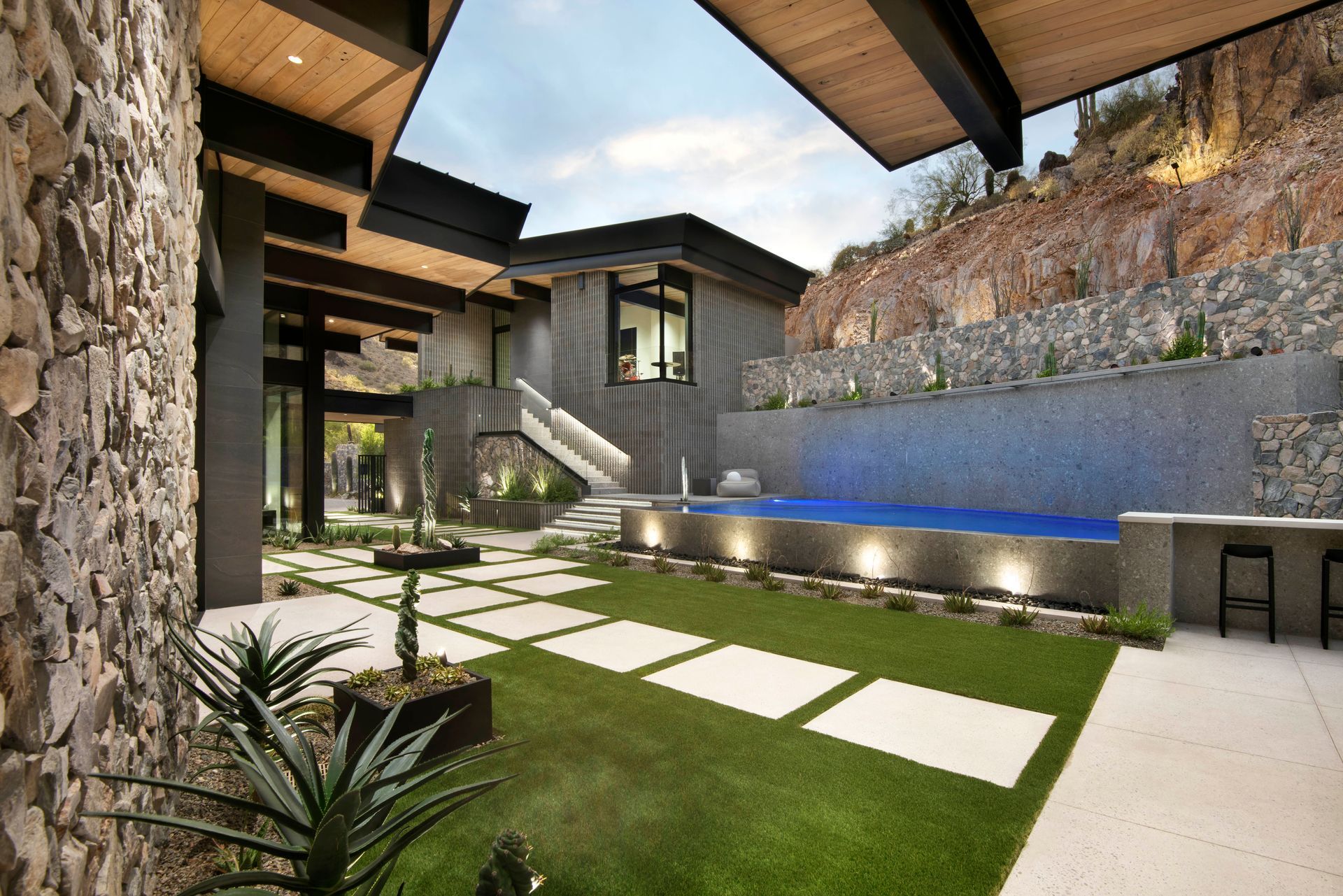 Modern home exterior with a pool, stone wall, and lush greenery.