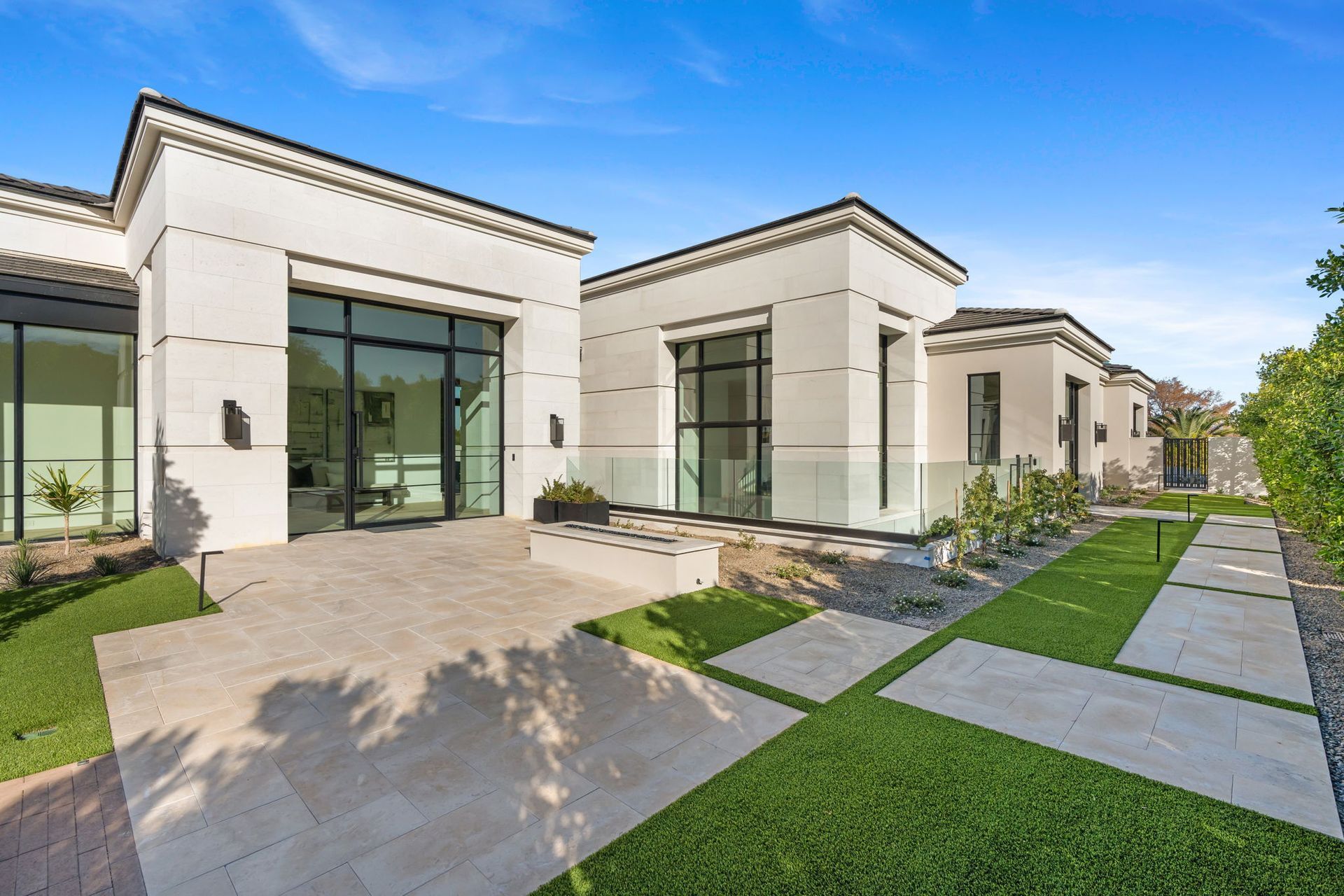 Modern white house with glass doors, pathway, and green lawn under a blue sky.