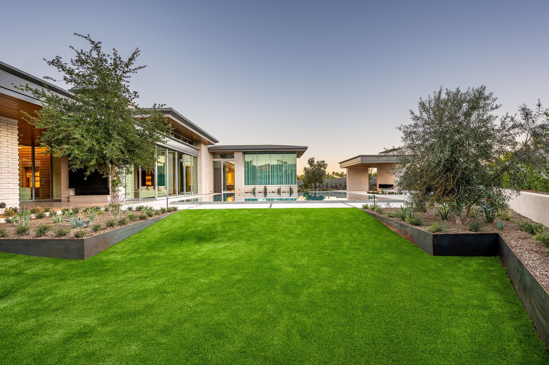 Backyard with green grass, modern house, trees, and a pool.