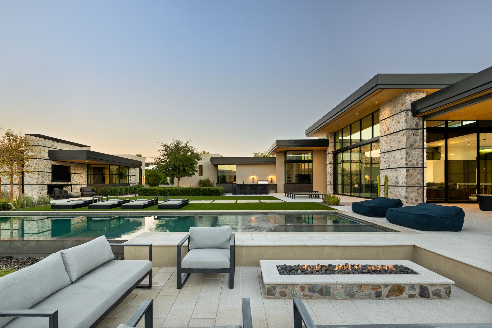 Modern luxury home exterior with pool, seating areas, and a fire pit.