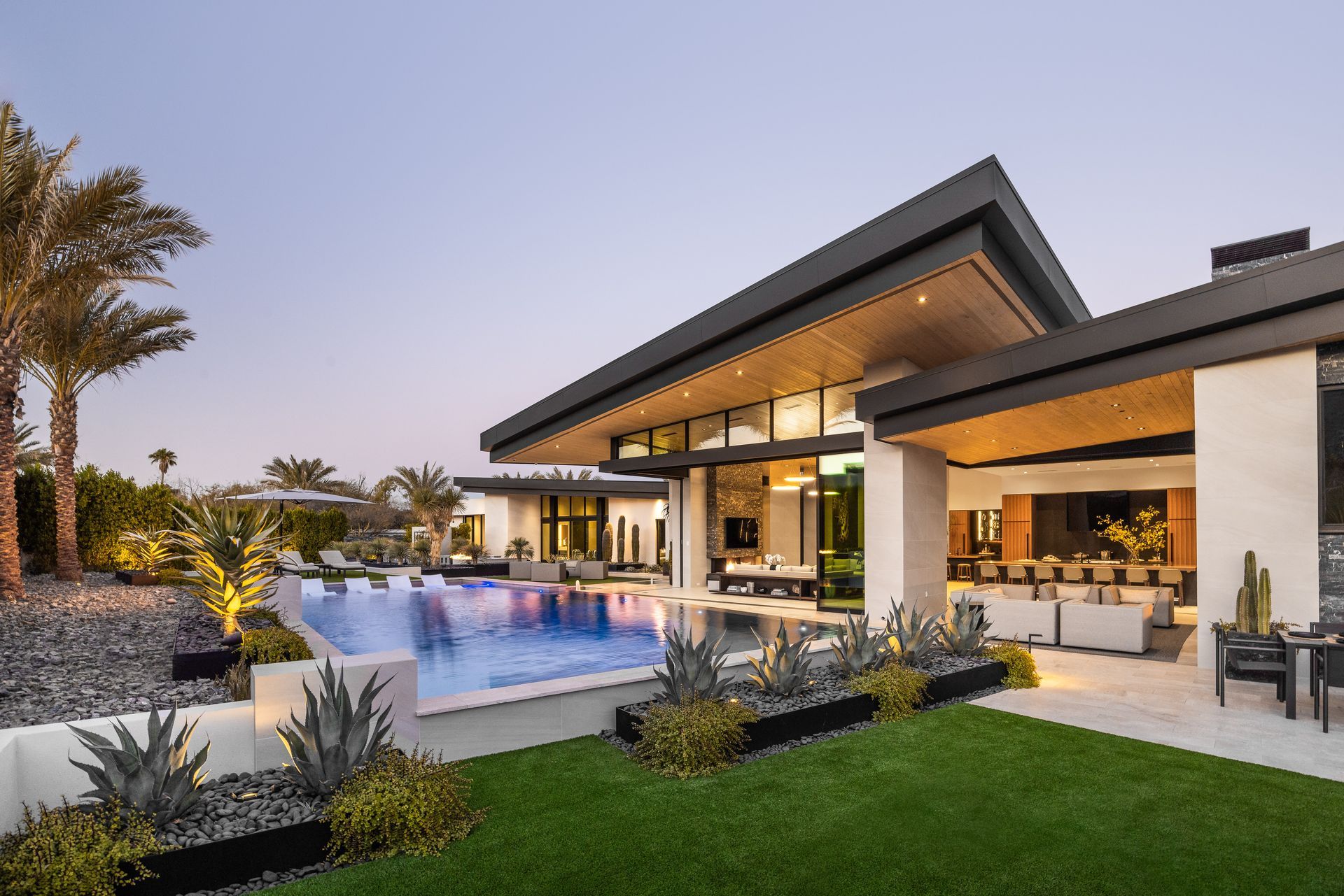 Modern luxury home with pool, lush landscaping, and evening lighting.