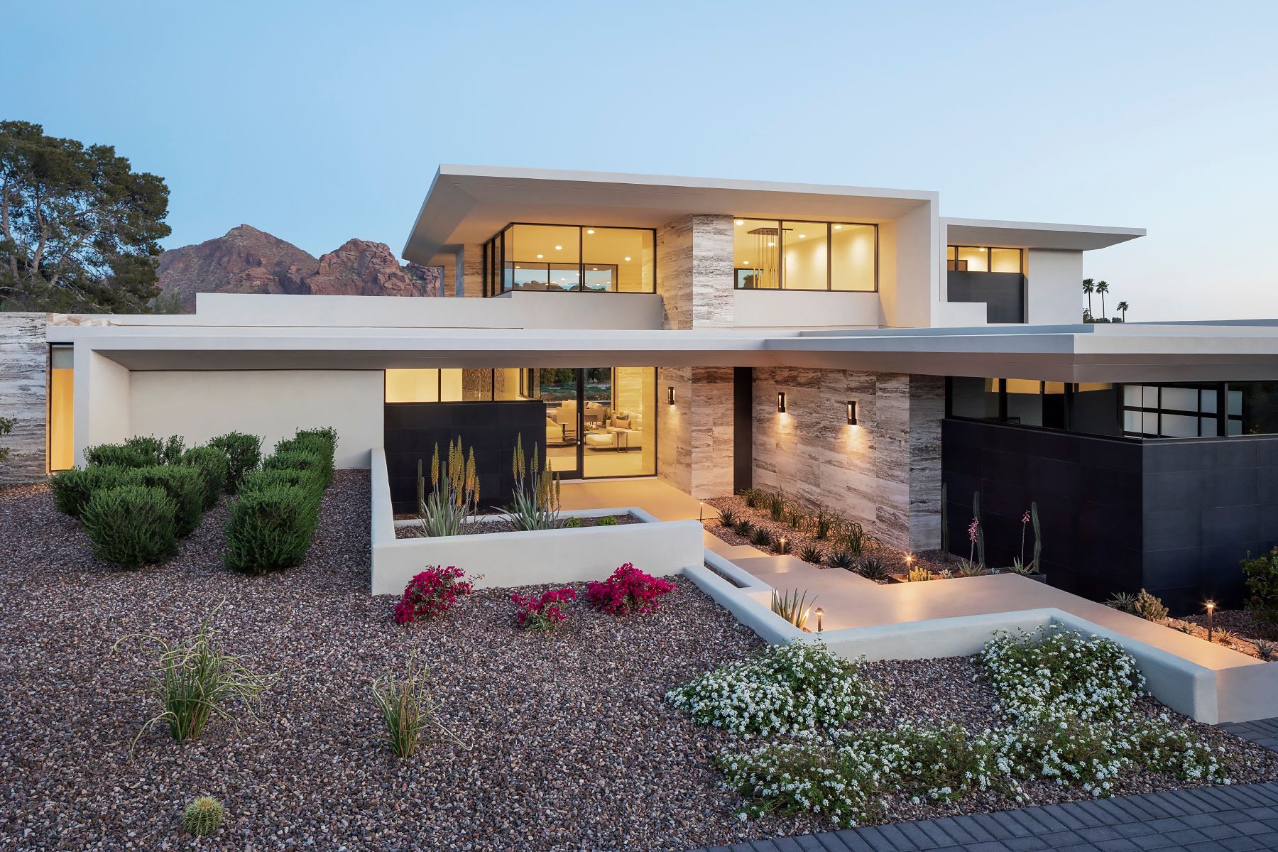 Modern home exterior with stone and stucco facade, front yard with landscaping and mountain backdrop.