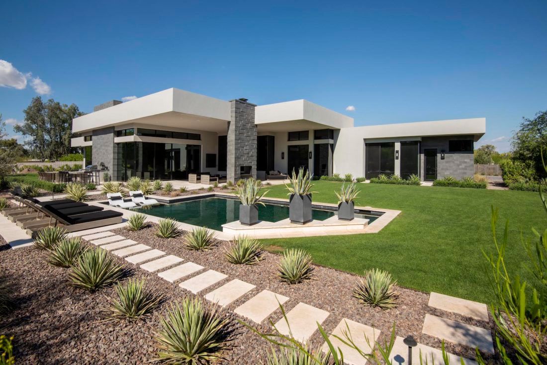 Modern home with a pool, pathway, and manicured lawn under a blue sky.