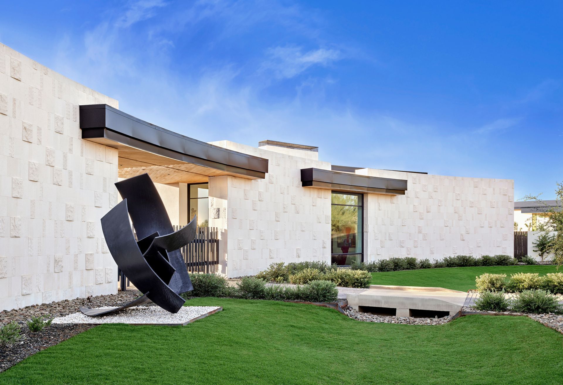 Modern home exterior with sculpture on manicured lawn under blue sky.