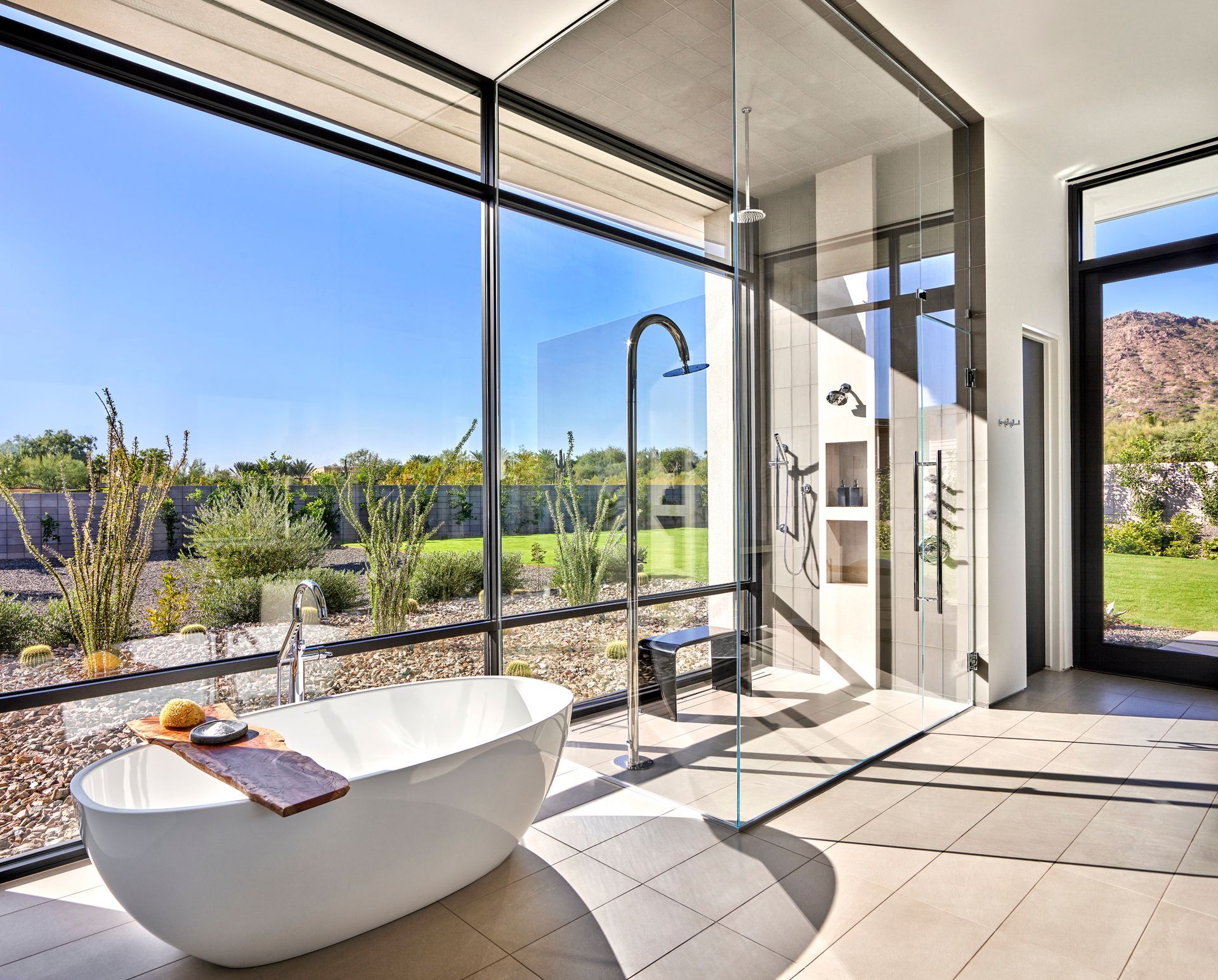 Luxurious bathroom with a soaking tub and a glass-walled shower with a view of a sunny backyard.