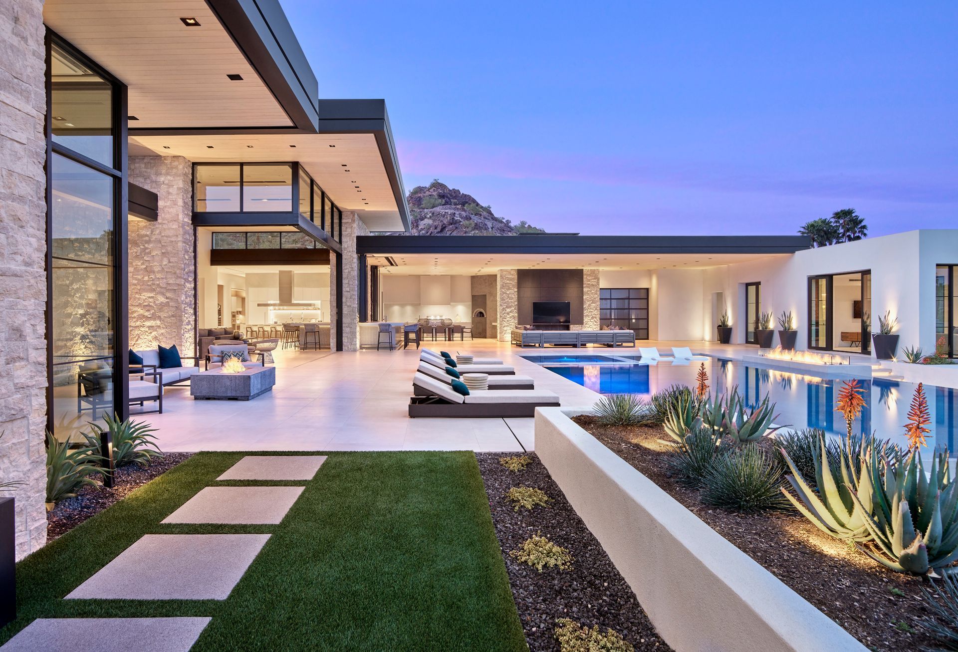 Modern luxury home exterior with pool, patio, and mountain backdrop at dusk.