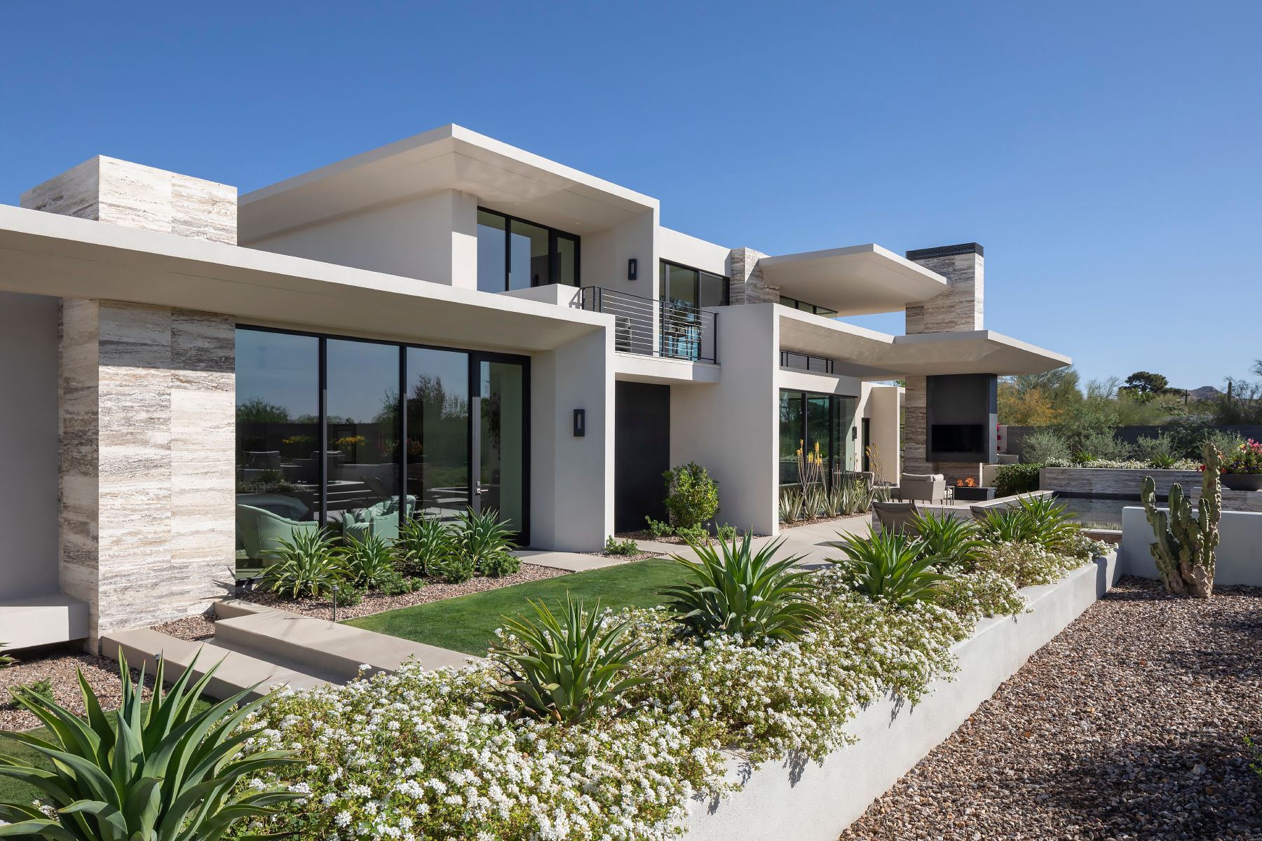 Modern white house with large windows, landscaping, and clear blue sky.